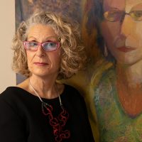 Woman with curly light blonde hair in front of a painting of a woman